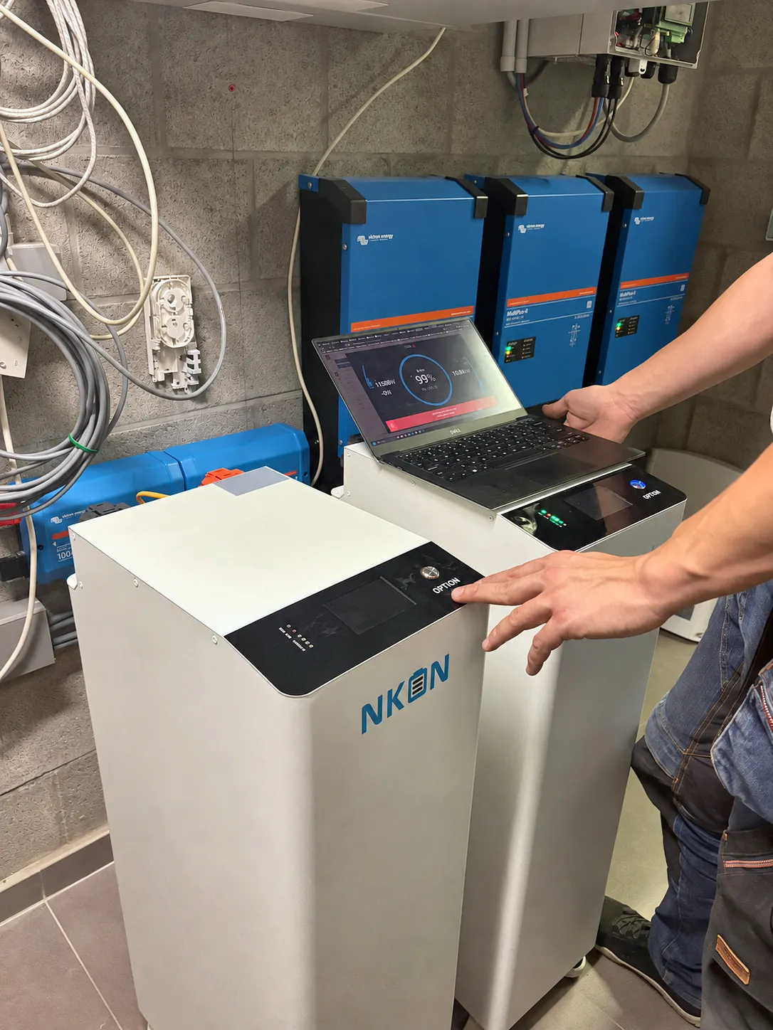A home battery being configured with a laptop, with the inverters on the wall above