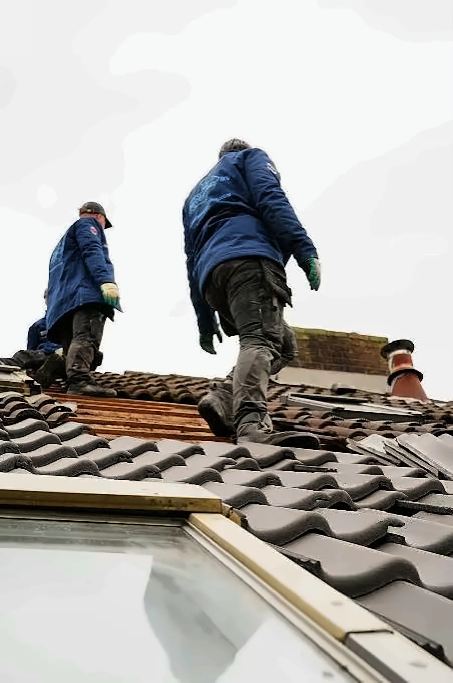 Réalisation : couvreurs sur un toit en tuiles pendant une rénovation de toiture, avec une fenêtre de toit au premier plan