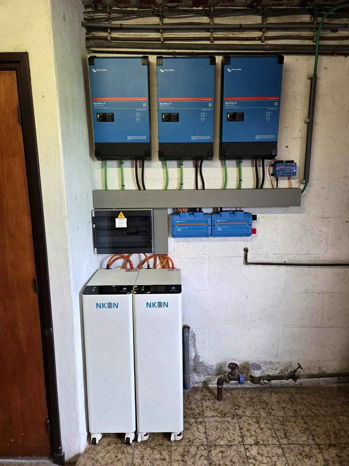 Drie omvormers met sturing aan de muur en twee thuisbatterijen eronder, in een technische ruimte